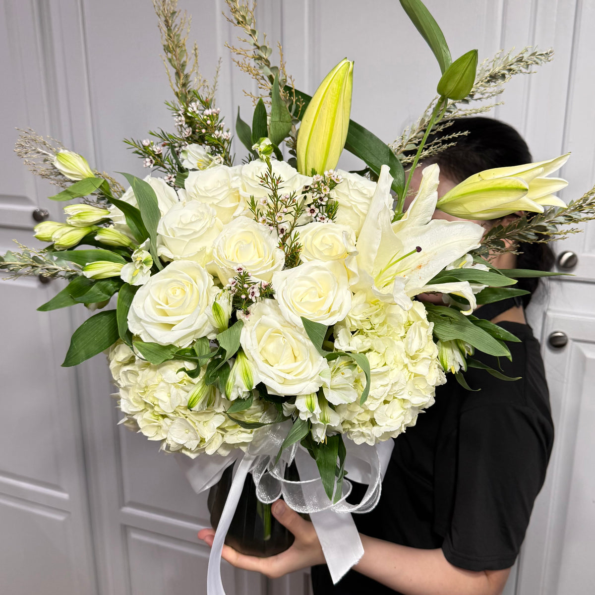 Large white floral arrangement with roses, lilies, and hydrangeas in a vase.
