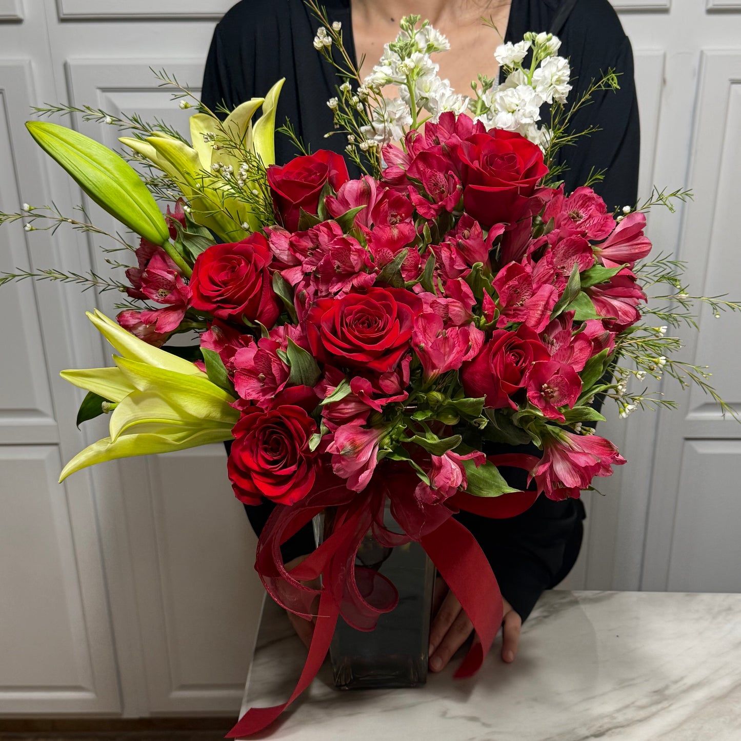 A person holds a lovely bouquet of red roses, pink alstroemeria, and yellow lilies.