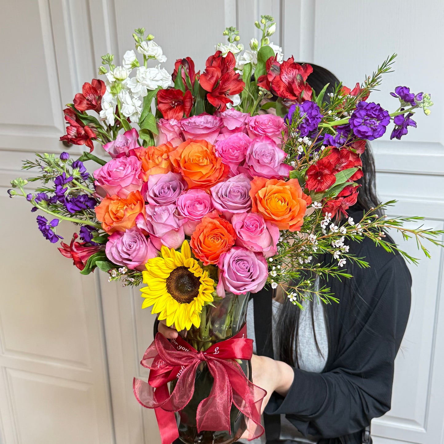Vibrant bouquet of roses, sunflower, and mixed flowers in a clear vase.