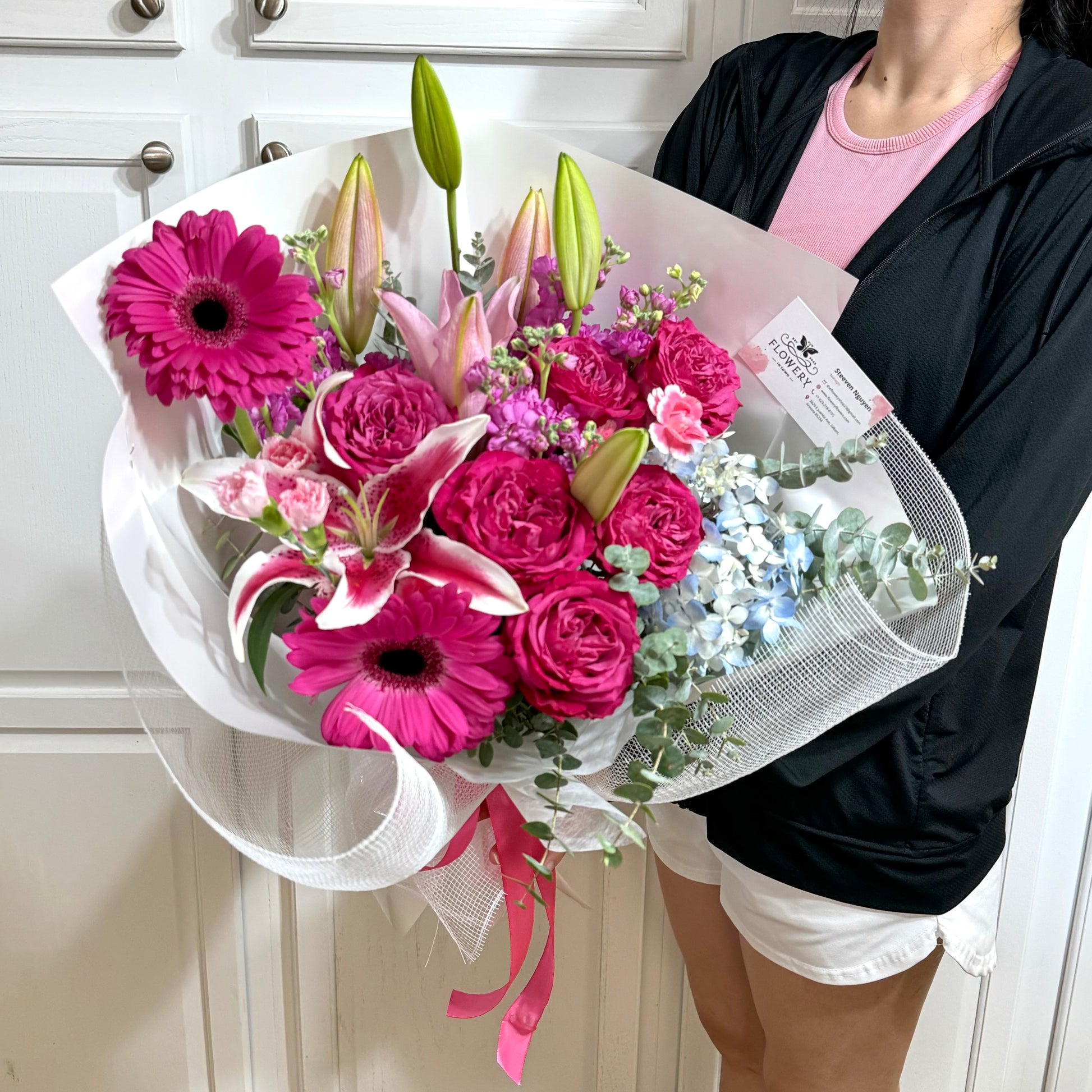 Vibrant pink lilies, roses, and daisies bouquet wrapped in white mesh.