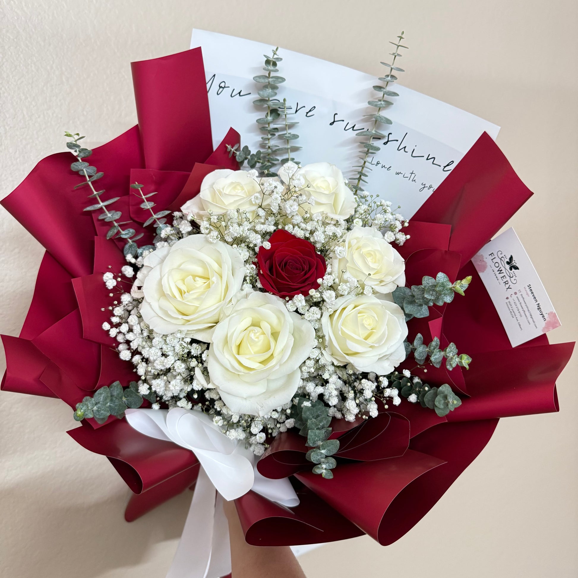 Elegant bouquet of white and red roses, baby's breath, and eucalyptus in red wrap.