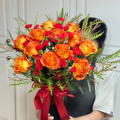 Vibrant orange and yellow rose bouquet with red accents and green foliage.