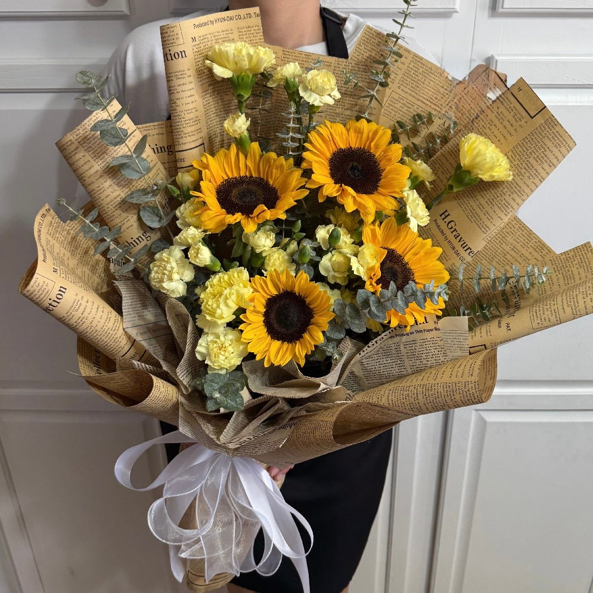 Elegant bouquet of sunflowers and yellow carnations in newspaper wrap.