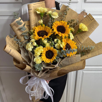 Elegant bouquet of sunflowers and yellow carnations in newspaper wrap.