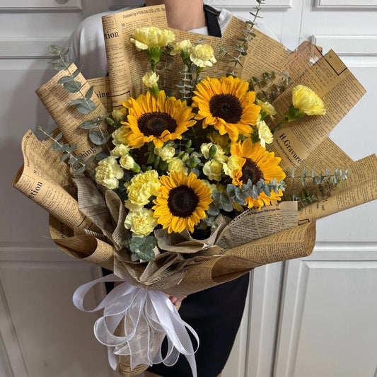Elegant bouquet of sunflowers and yellow carnations in newspaper wrap.