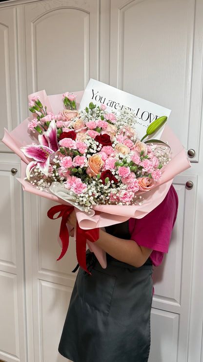 Large pink-wrapped bouquet of pink, red, and peach flowers with a red ribbon.