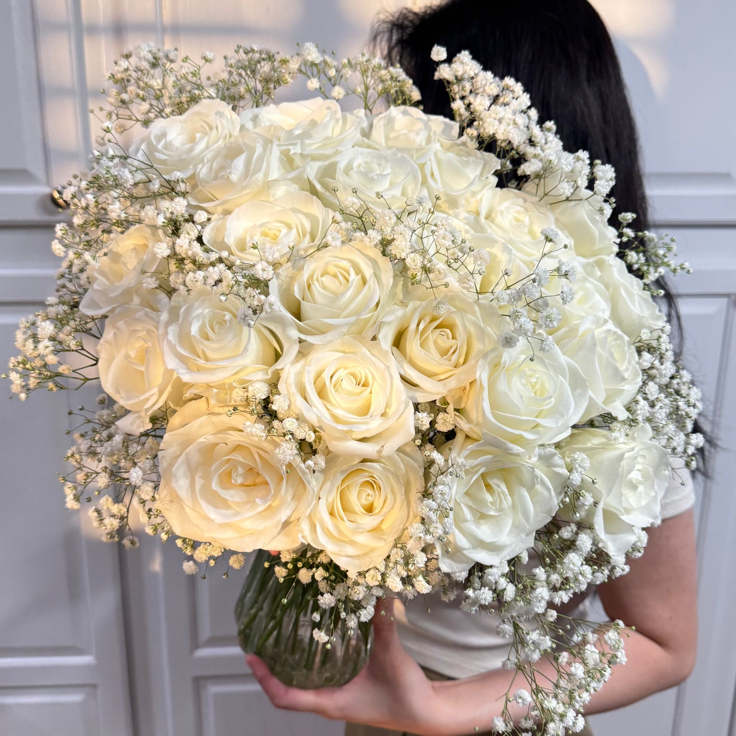 Lush bouquet of white roses and baby's breath in a clear glass vase.