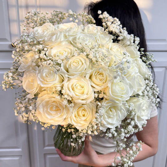 Lush bouquet of white roses and baby's breath in a clear glass vase.