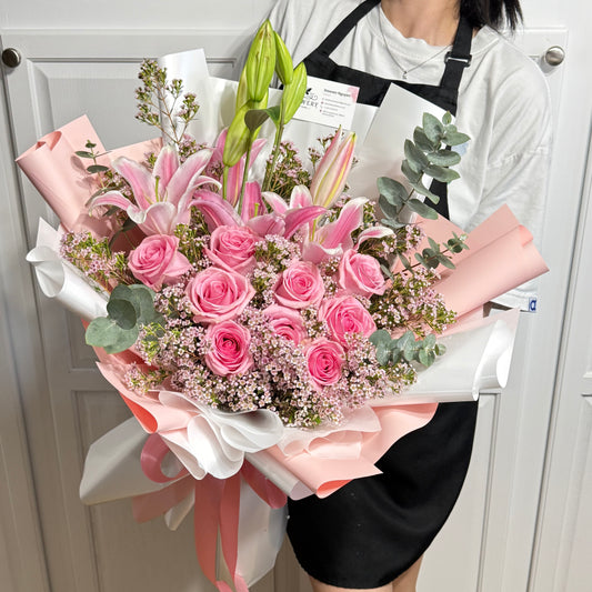 Vibrant pink rose and lily bouquet with eucalyptus, wrapped in pink and white paper.
