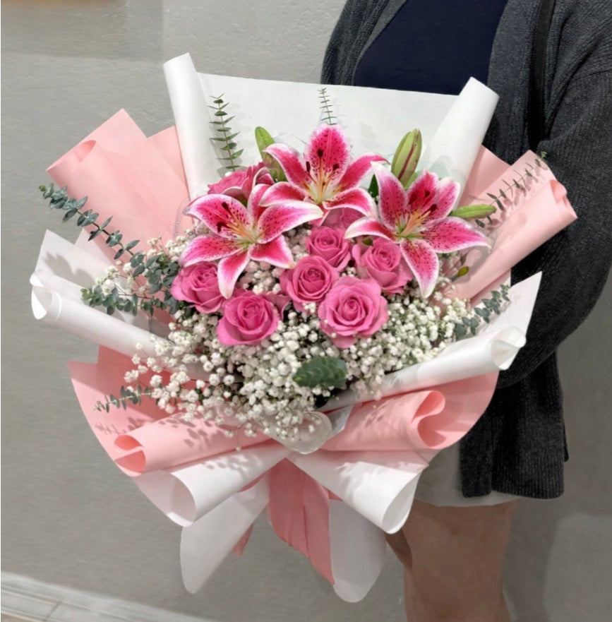 Pink lilies and roses bouquet with baby's breath, wrapped in pink and white paper.