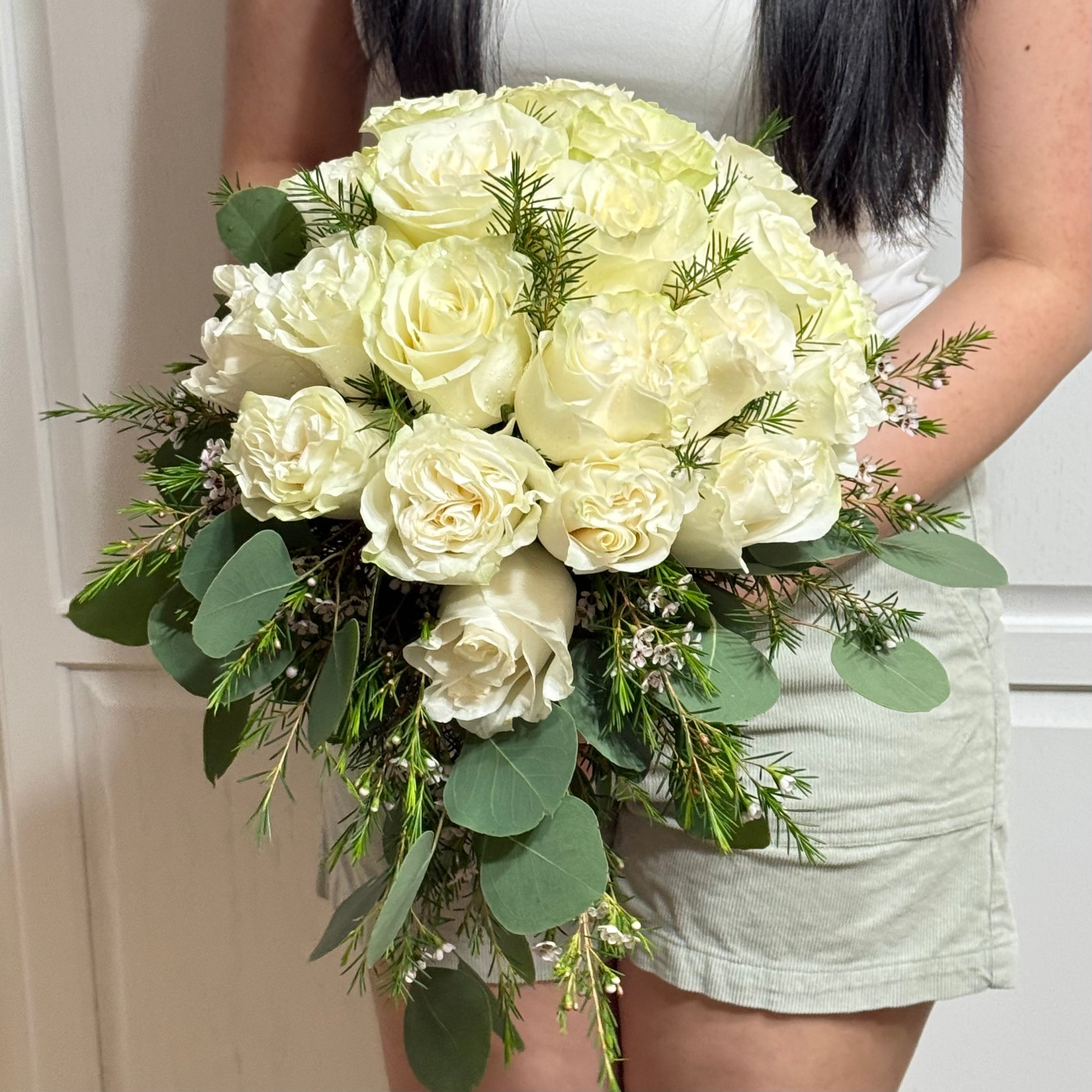 A person holds a cascading bouquet of white roses, eucalyptus, and green foliage.