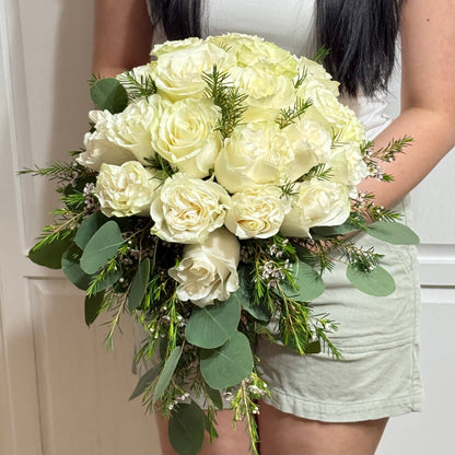 A person holds a cascading bouquet of white roses, eucalyptus, and green foliage.