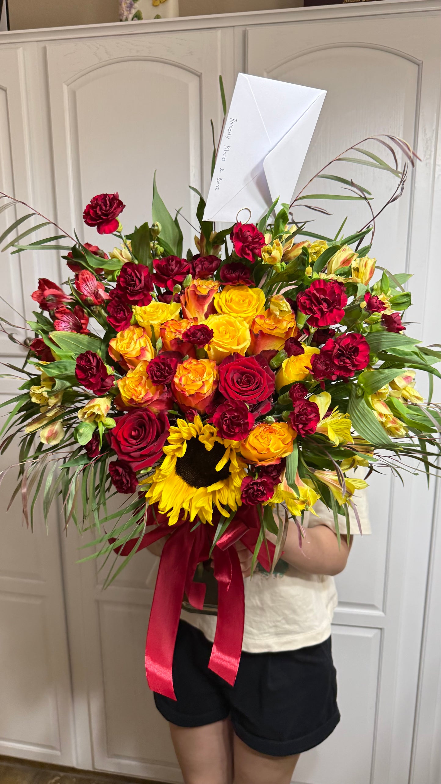 Bright bouquet of red, yellow, orange flowers, sunflower, and green foliage.