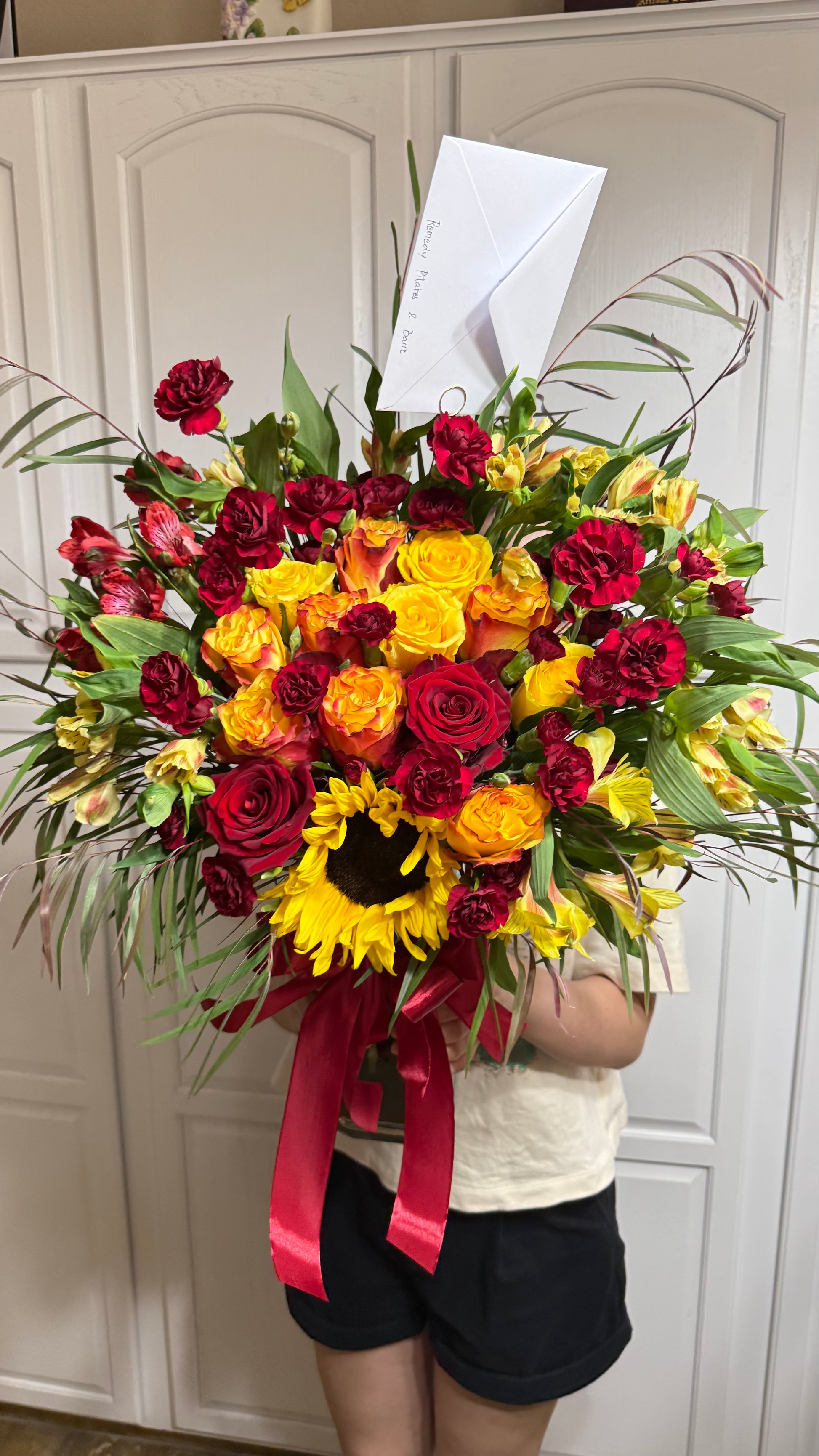 Bright bouquet of red, yellow, orange flowers, sunflower, and green foliage.