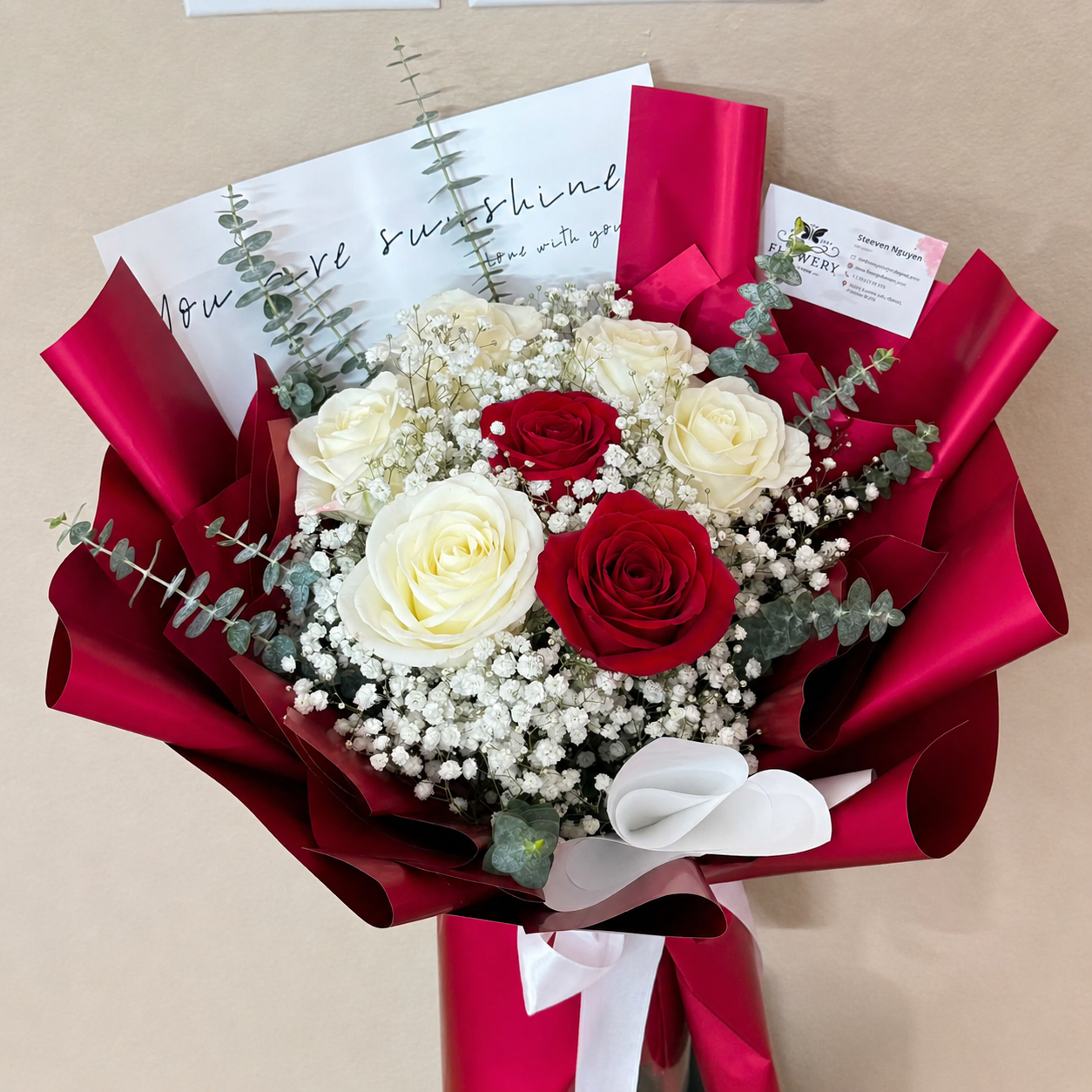 Elegant red and white rose bouquet with baby's breath, wrapped in glossy red paper.