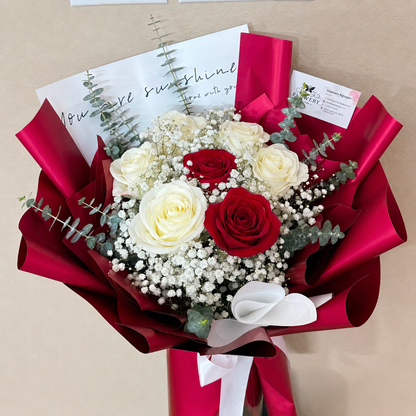 Elegant red and white rose bouquet with baby's breath, wrapped in glossy red paper.