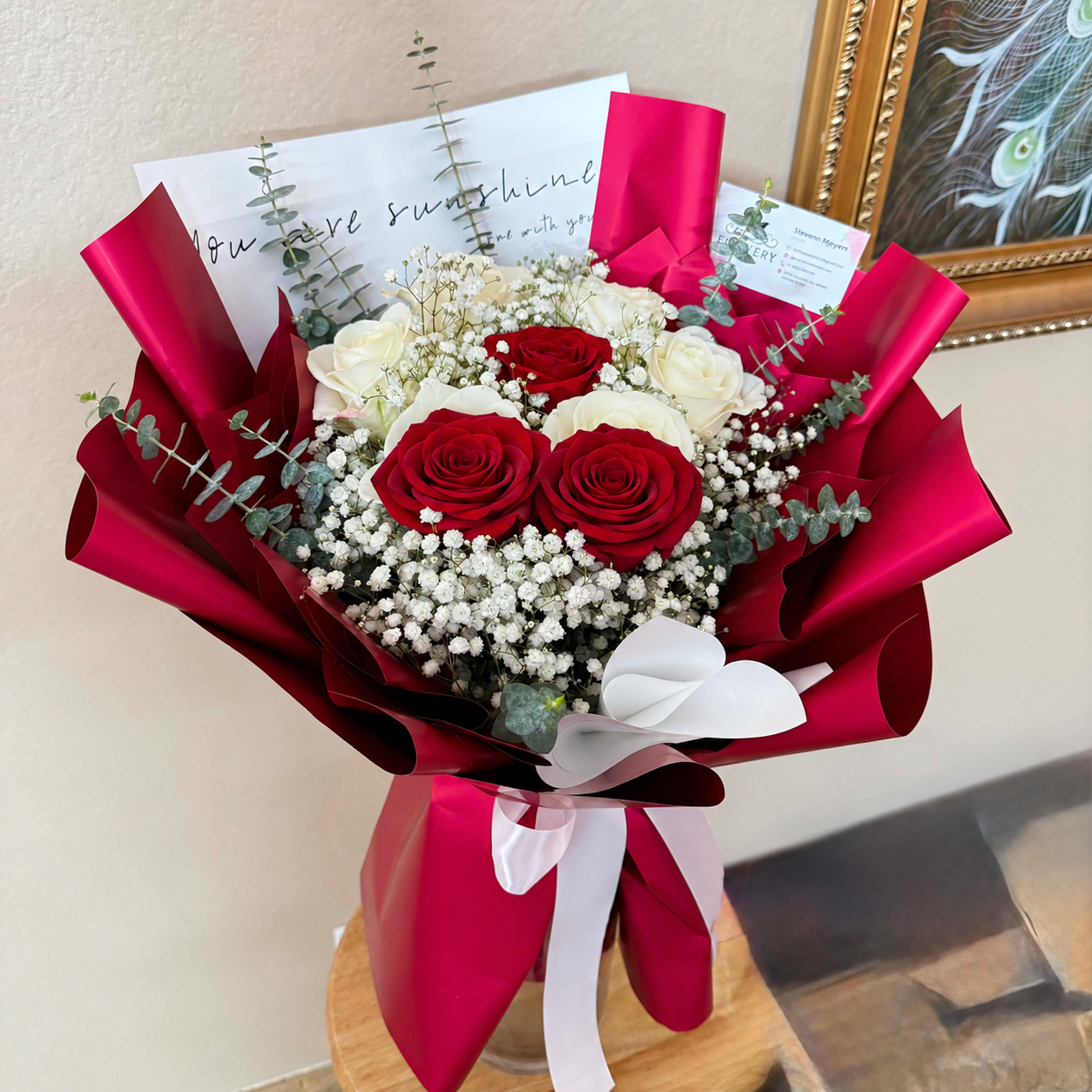 A dreamy bouquet of red and white roses, baby's breath, and eucalyptus in red wrap.