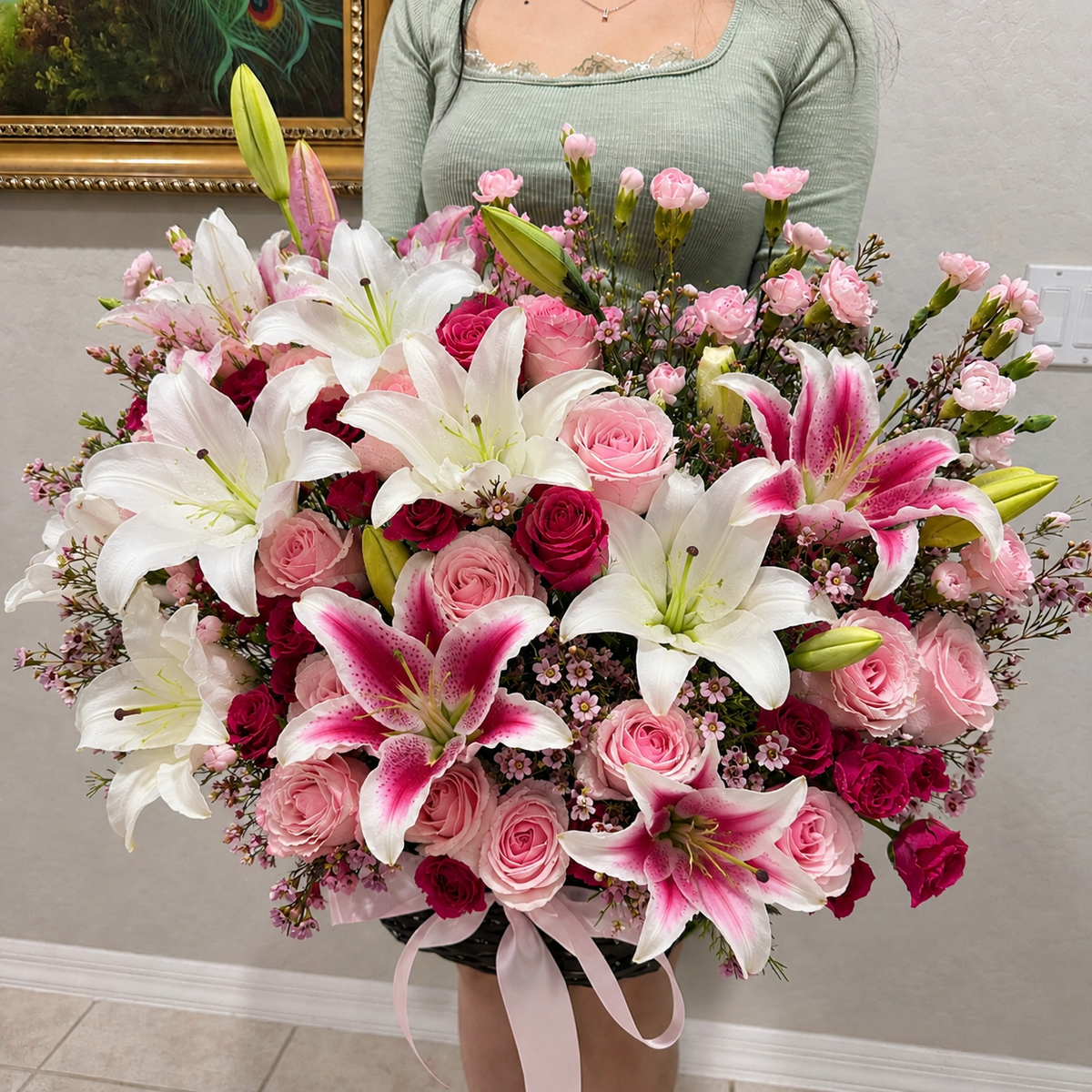 A large, vibrant bouquet of white and pink lilies and roses with a pink ribbon.