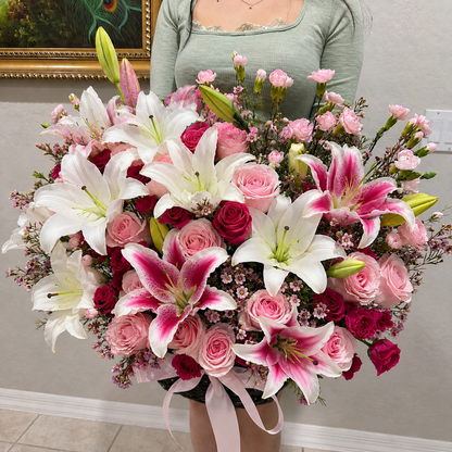 A large, vibrant bouquet of white and pink lilies and roses with a pink ribbon.