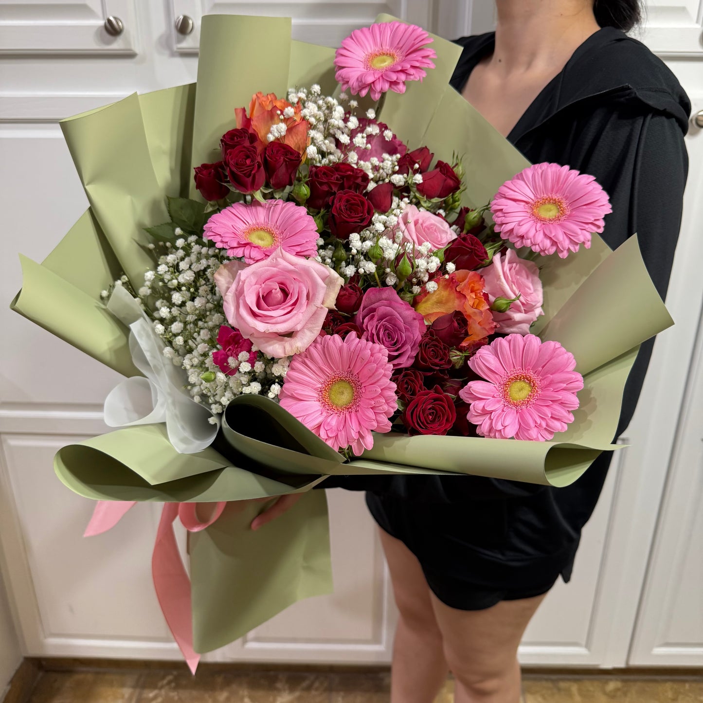 Large bouquet of pink, red, and orange roses with pink gerberas and baby's breath.