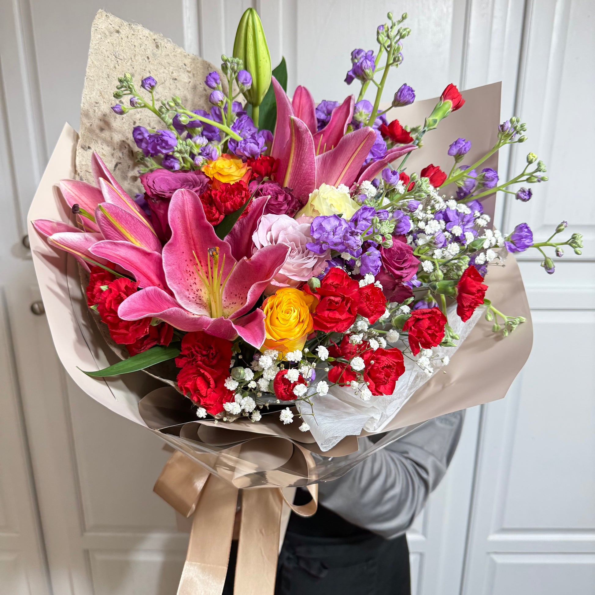 Vibrant bouquet with pink lilies, red carnations, yellow roses, and purple flowers.