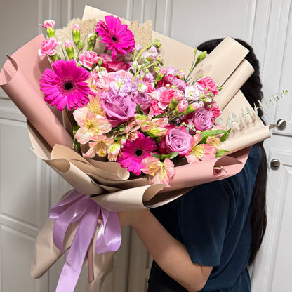 Vibrant pink and purple floral bouquet with gerberas, roses, and alstroemeria, wrapped in paper.
