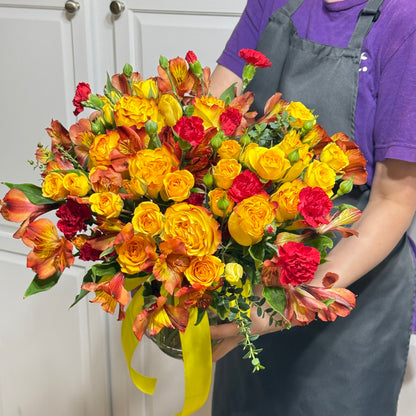 Bright yellow and red floral bouquet with a yellow ribbon, held by a person.