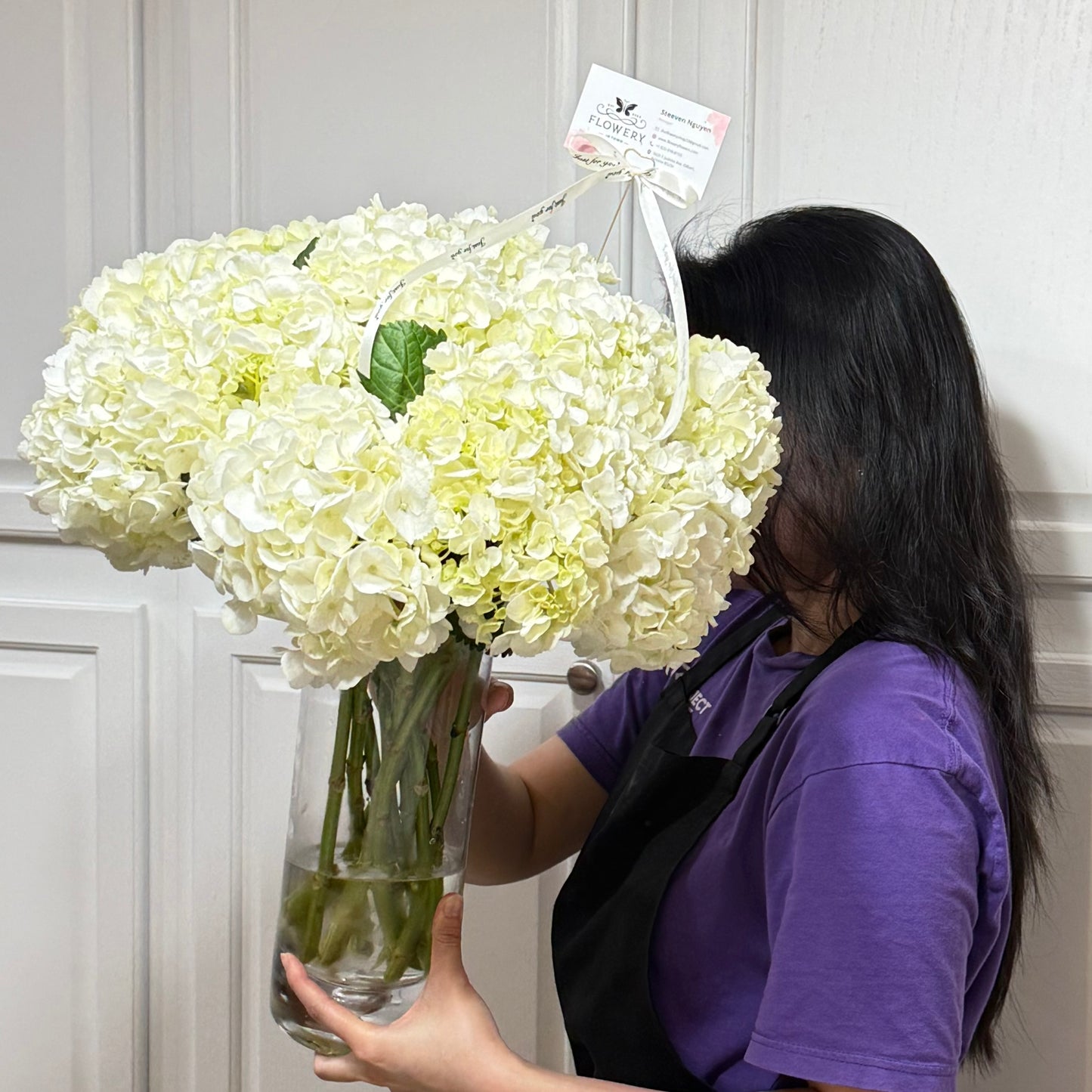 A person holds a large vase of fluffy white snowball hydrangeas.