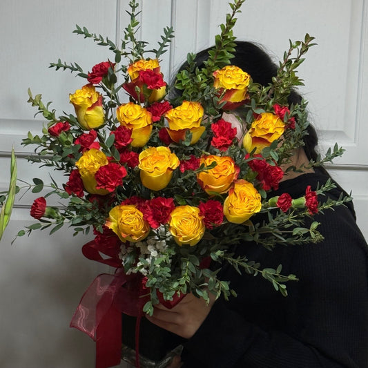 Large bouquet of vibrant yellow roses, red carnations, and green foliage with a red ribbon.