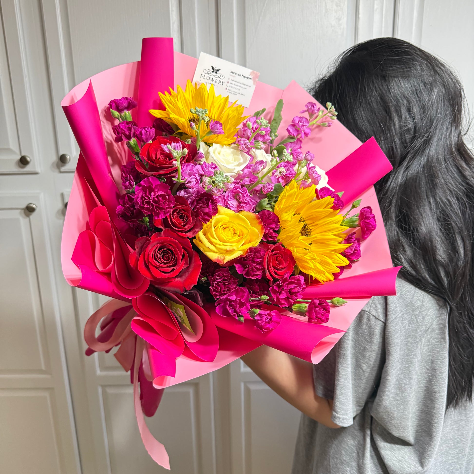 Vibrant pink bouquet featuring red roses, yellow sunflowers, and purple flowers.