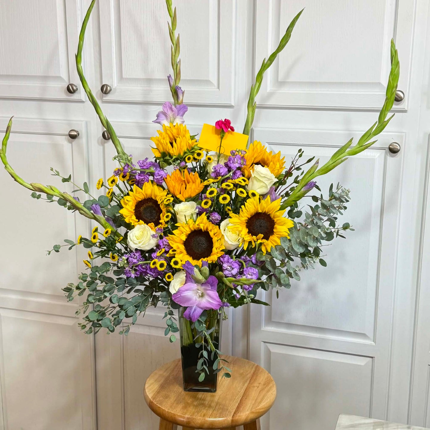 Vibrant bouquet of sunflowers, white roses, and purple flowers with tall green gladiolus.