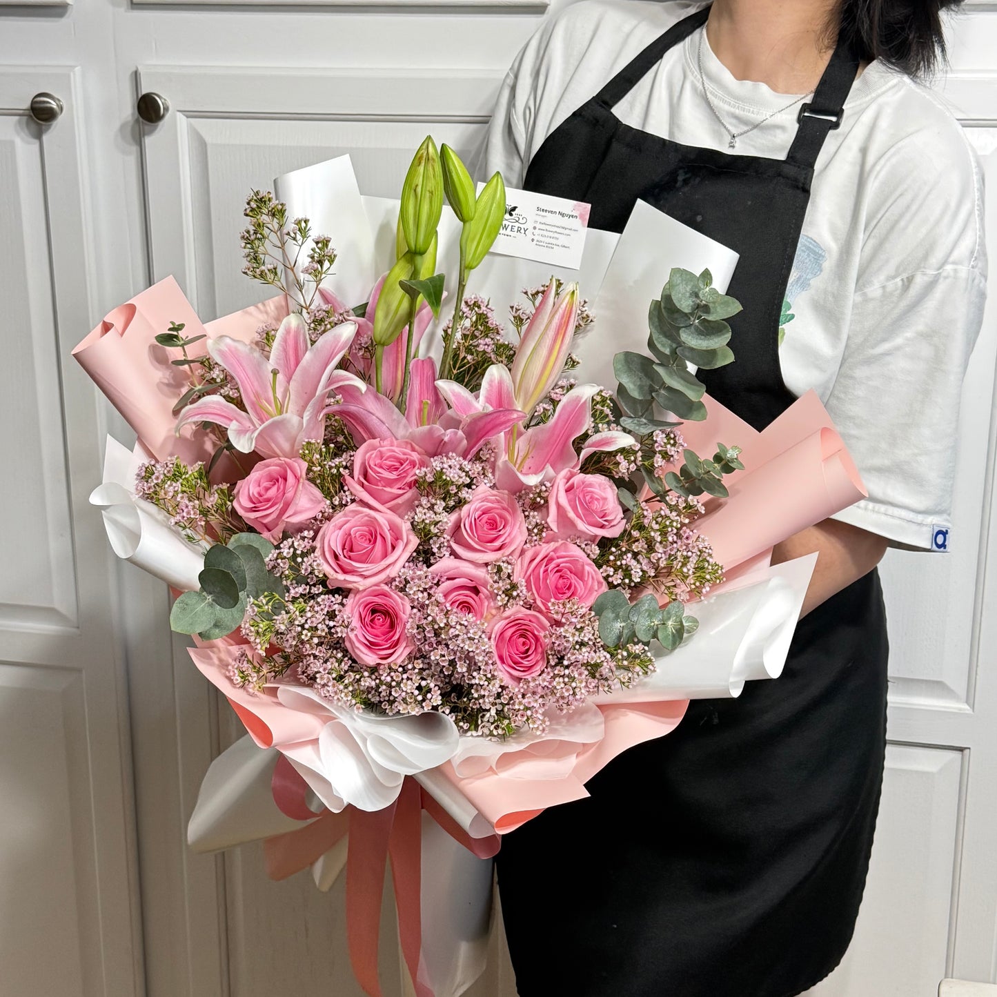 Large pink rose and lily bouquet with green foliage, wrapped in pink and white.
