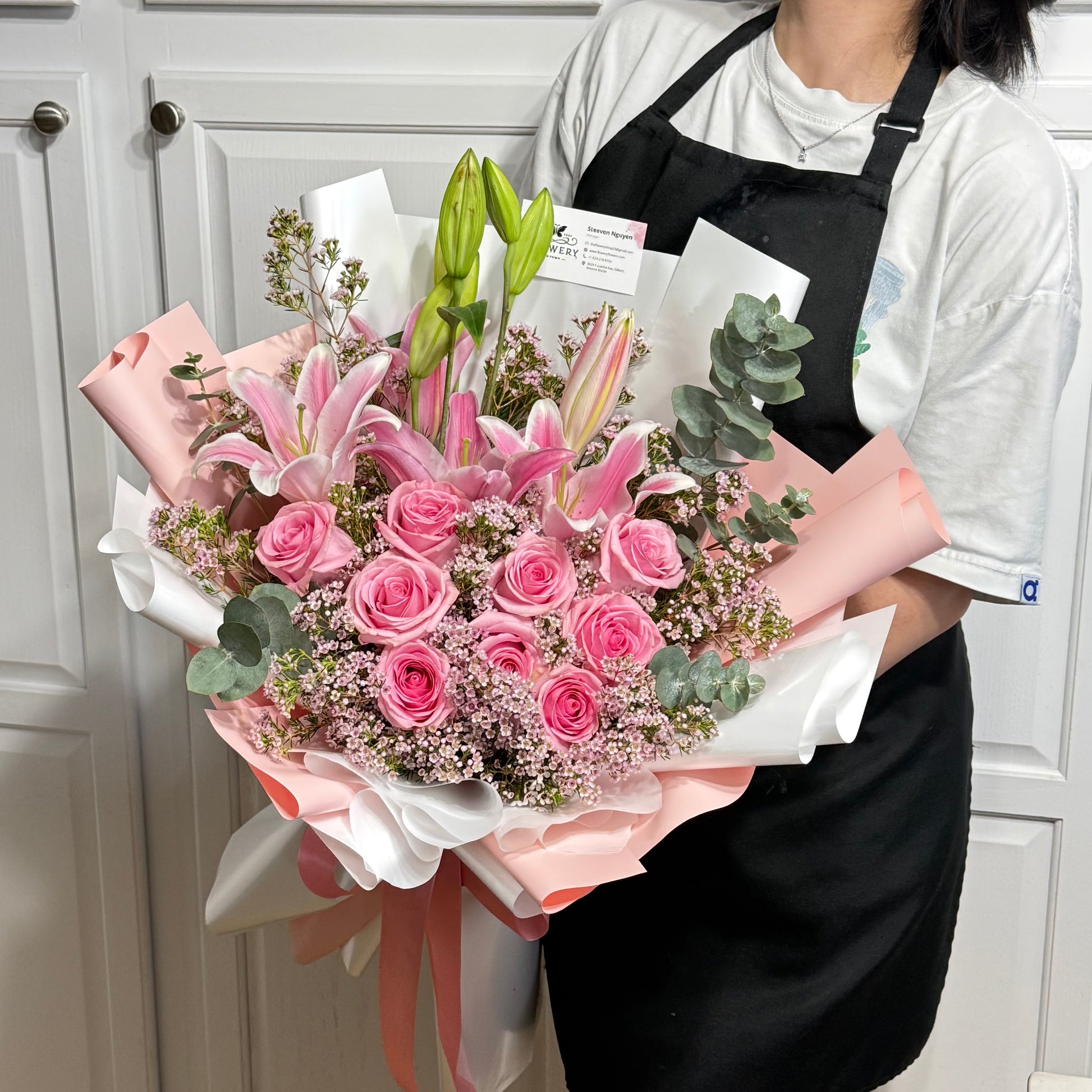 Large pink rose and lily bouquet with green foliage, wrapped in pink and white.
