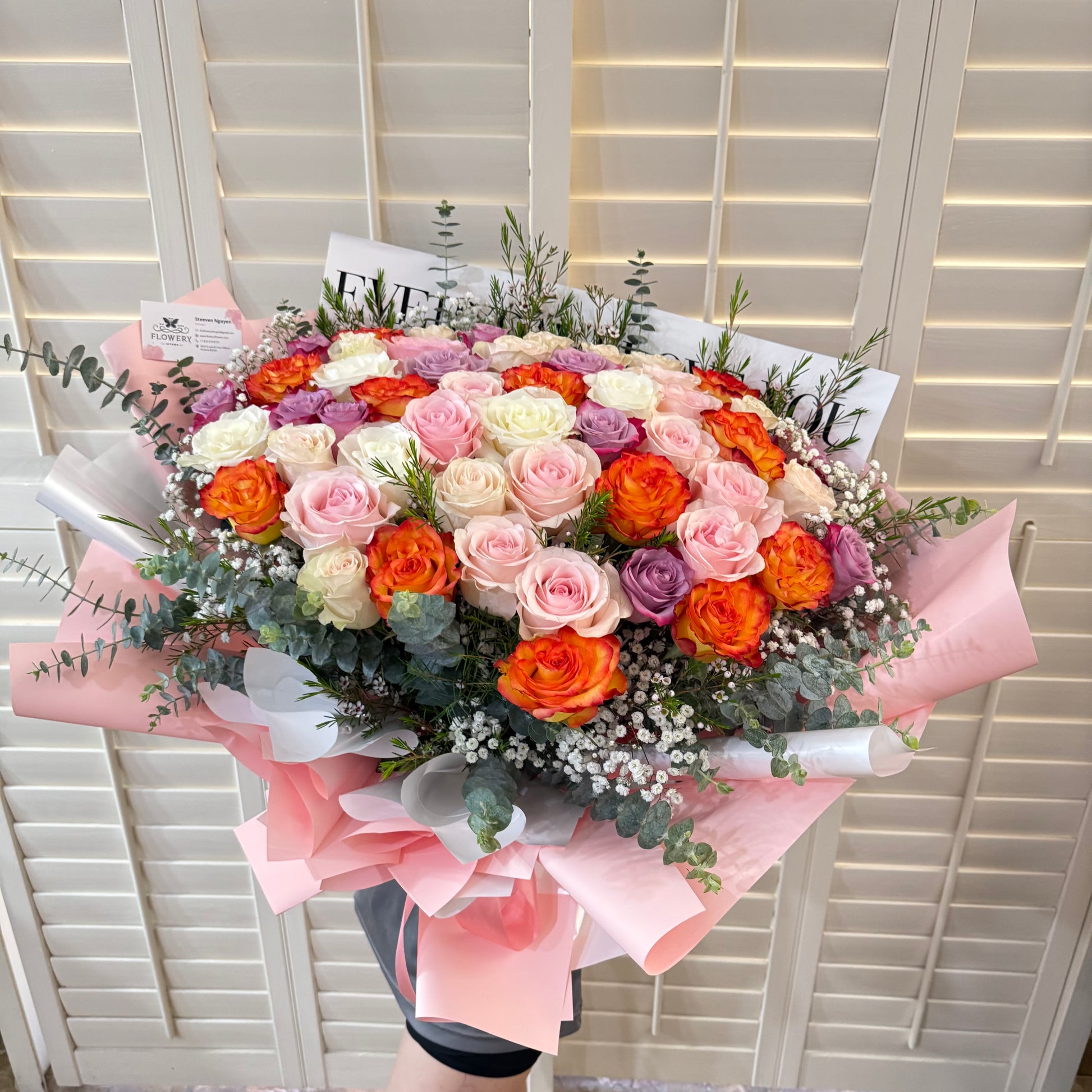 Large, colorful bouquet of pink, orange, white, and purple roses with greenery.
