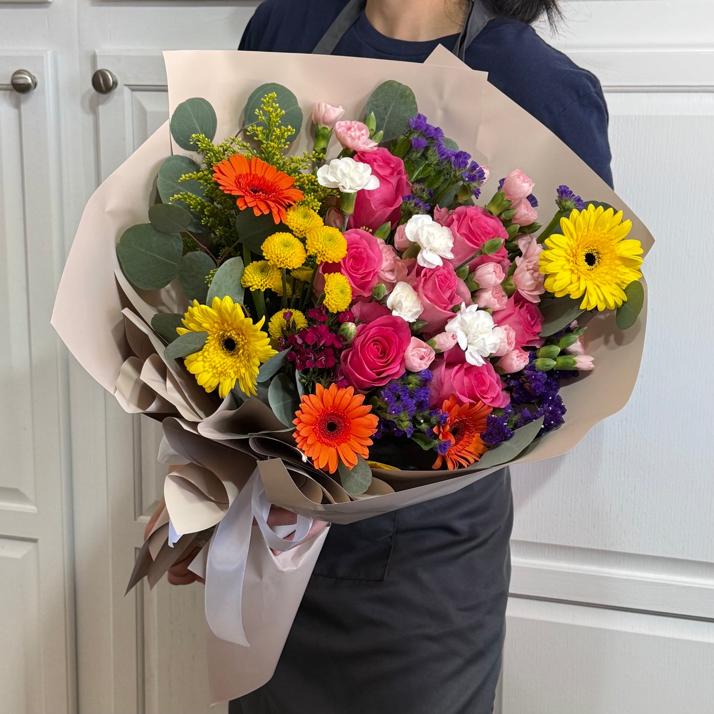 Vibrant bouquet with pink roses, orange, yellow daisies, and eucalyptus leaves.