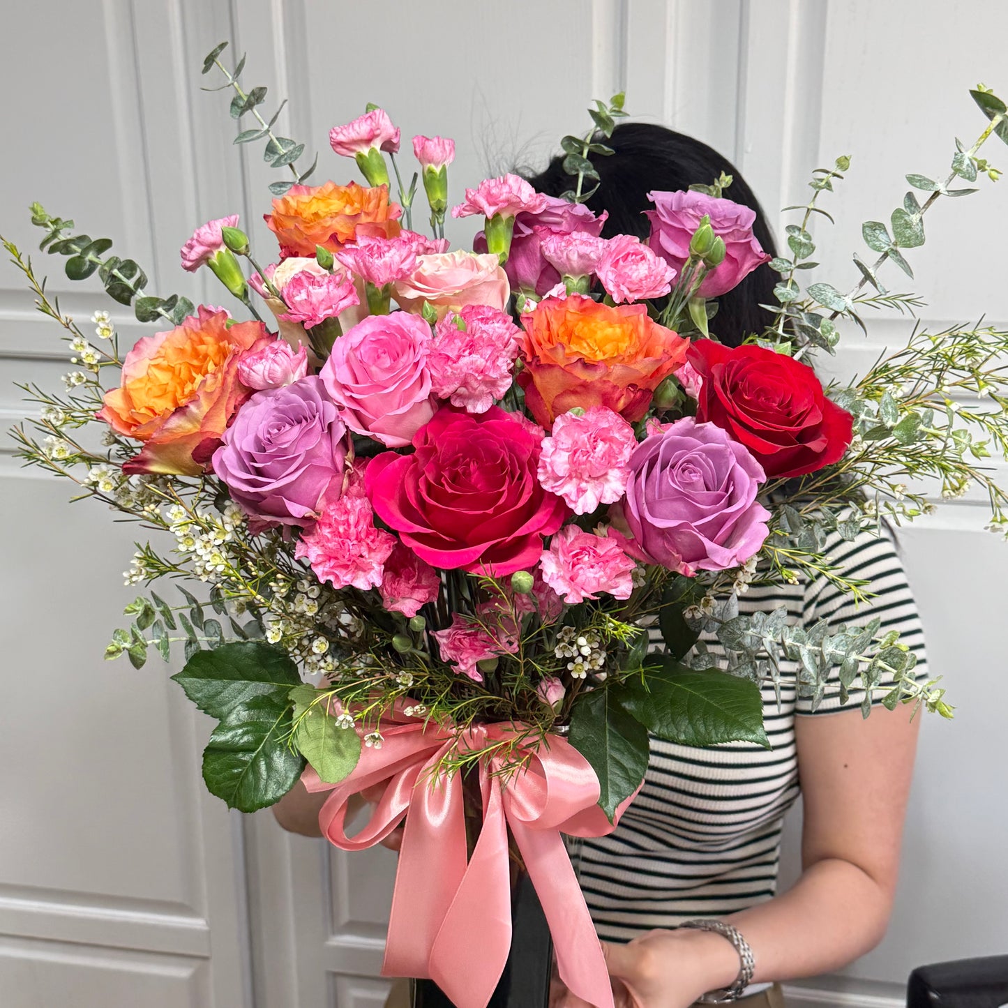 Vibrant bouquet of pink, orange, purple, and red roses with sprinkled white flowers.