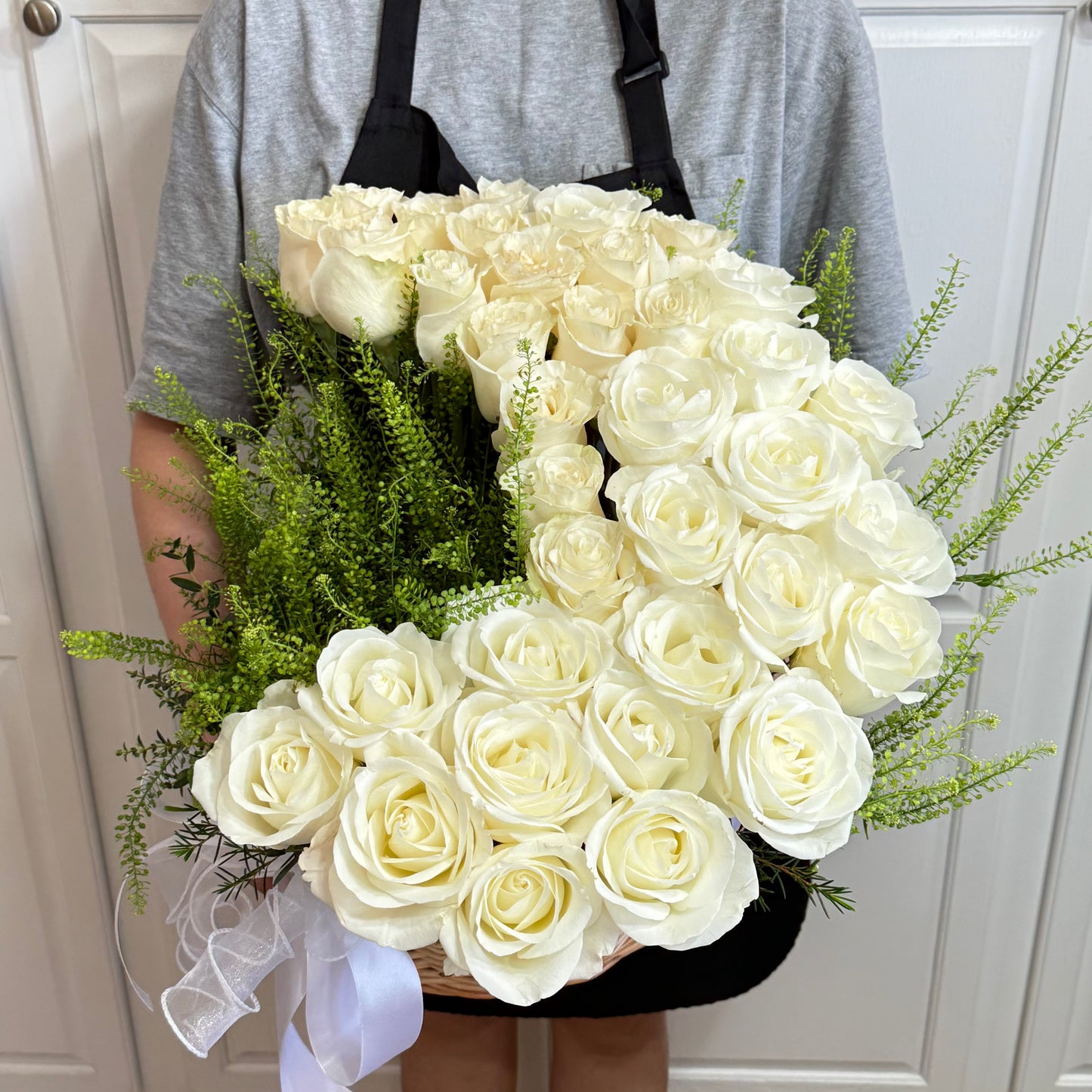 Large woven basket of creamy white roses, green foliage, and a white ribbon.
