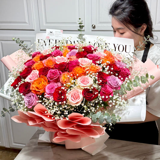 A woman holds a large bouquet of vibrant red, pink, and orange roses.