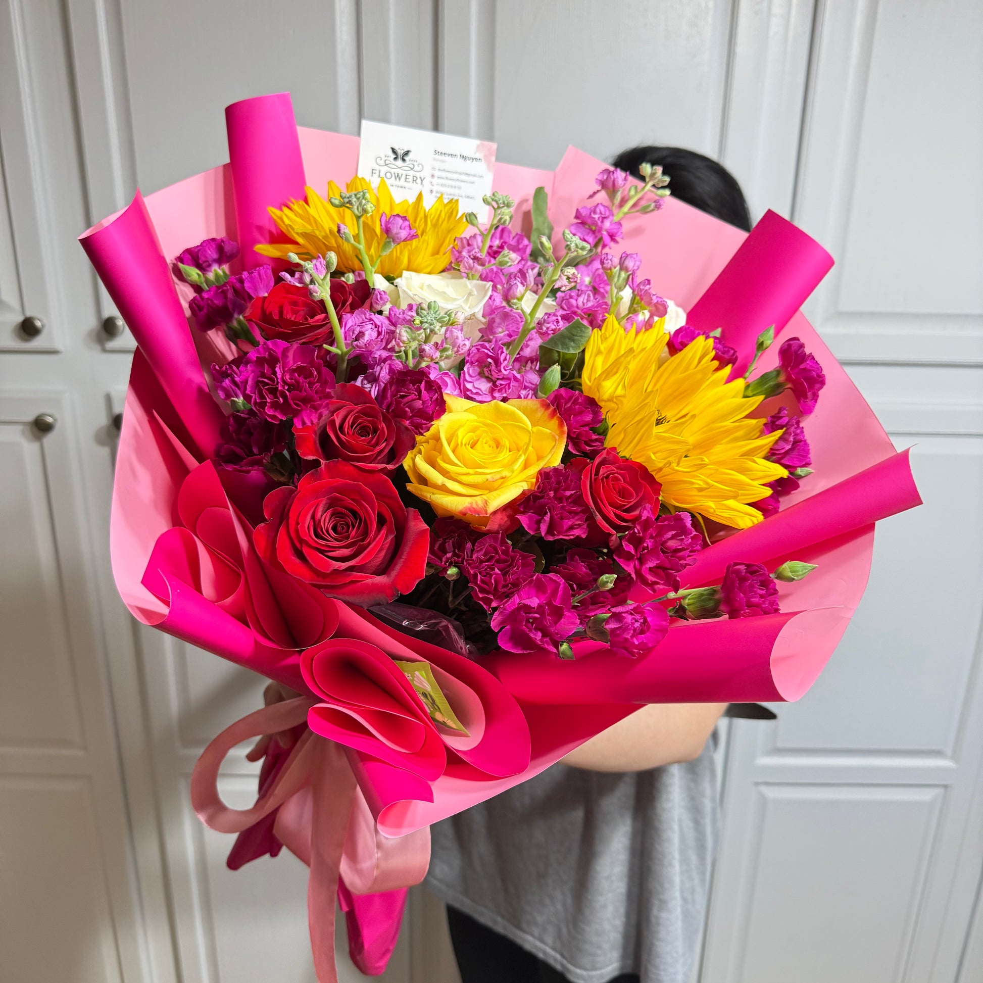 Vibrant bouquet of red roses, yellow blooms, and purple flowers in pink wrap.