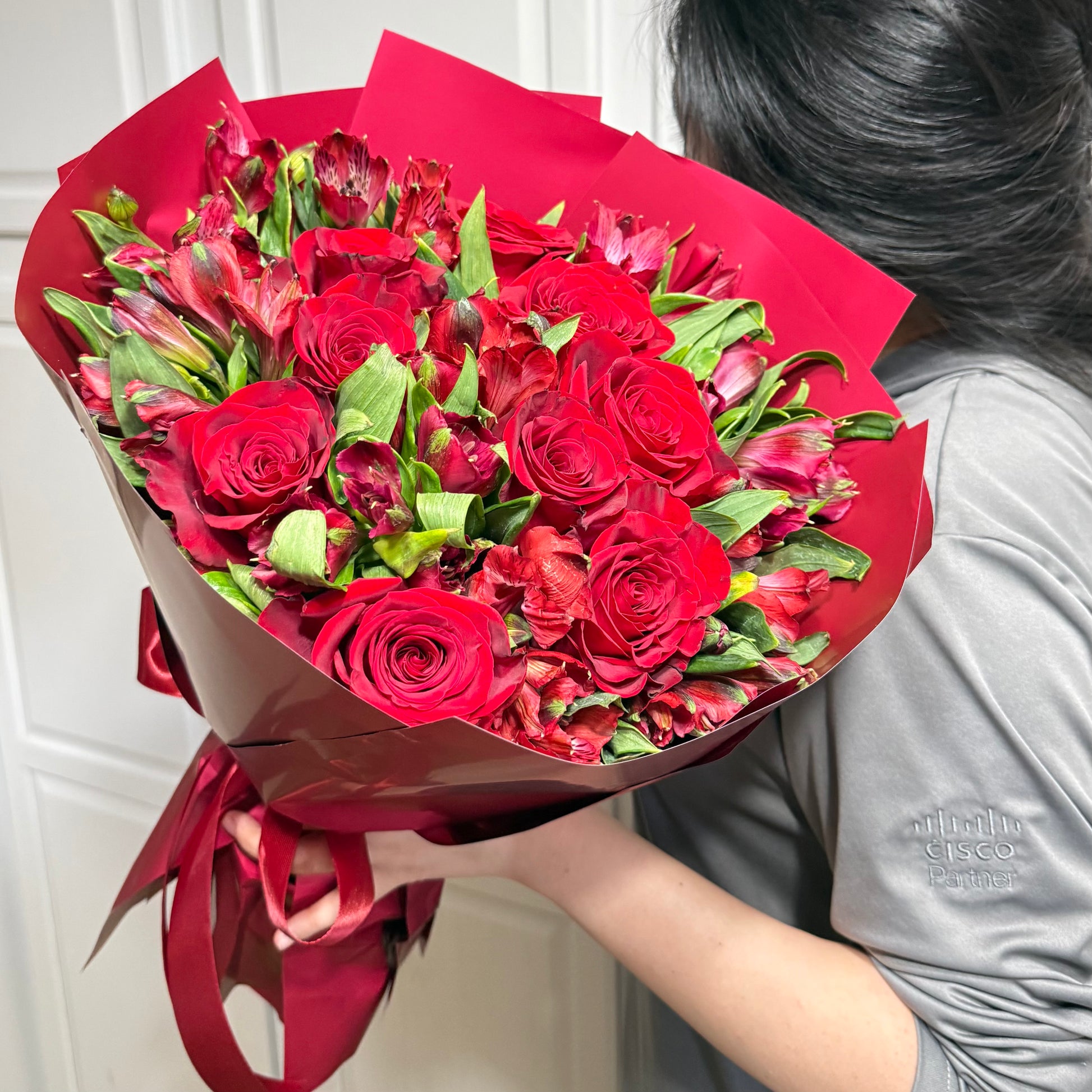 Vibrant bouquet of red roses and crimson flowers wrapped in red paper.