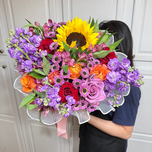 Vibrant mixed flower bouquet with a large yellow sunflower, red, orange, and purple blooms.