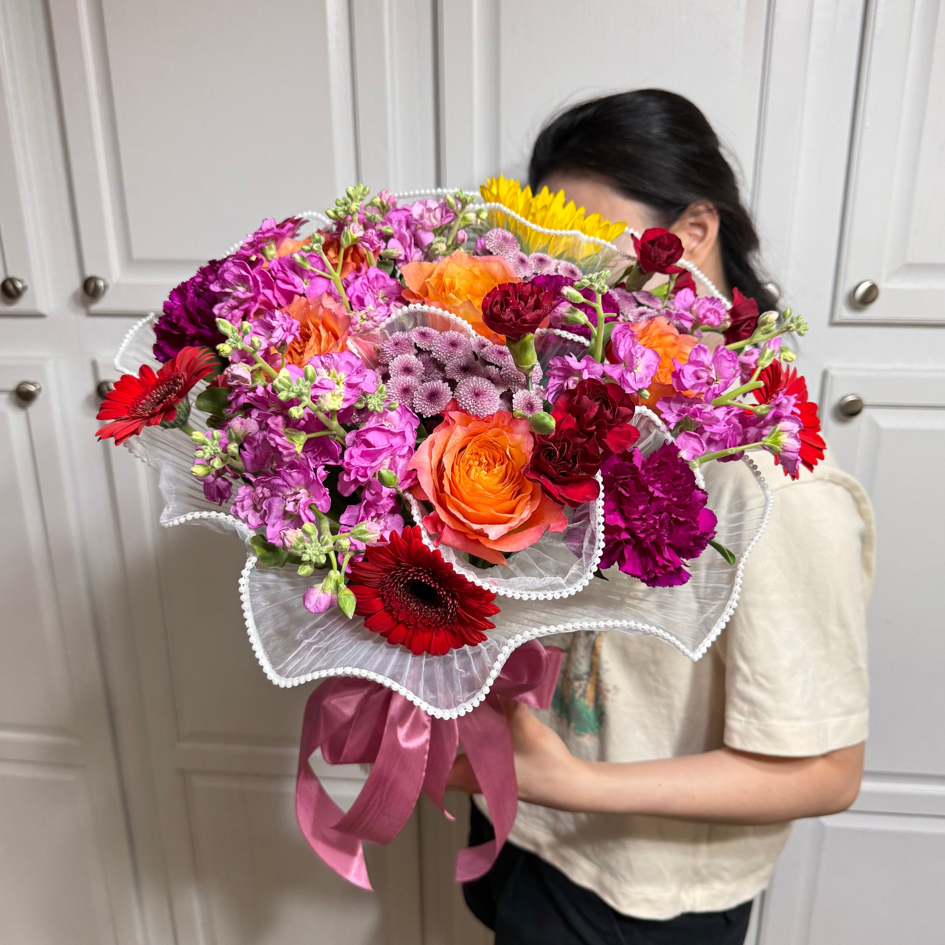 Vibrant mixed flower bouquet with orange, red, purple blooms and pink ribbon.