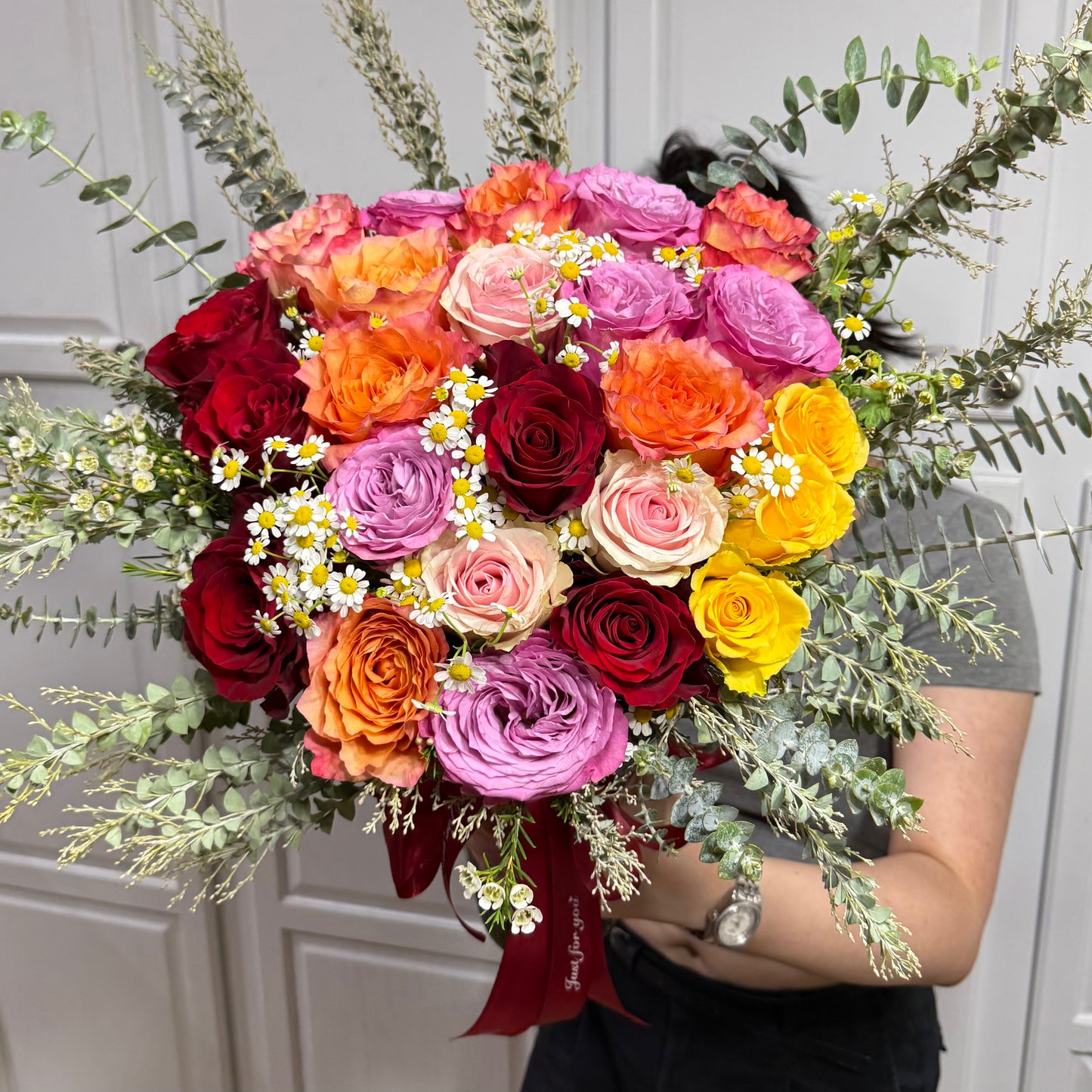 A vibrant bouquet of multi-colored roses, daisies, and eucalyptus leaves.