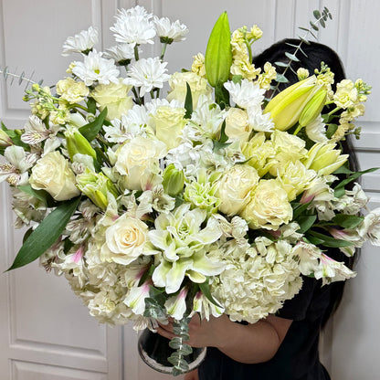 Lush white and cream floral arrangement with roses, lilies, and hydrangeas.